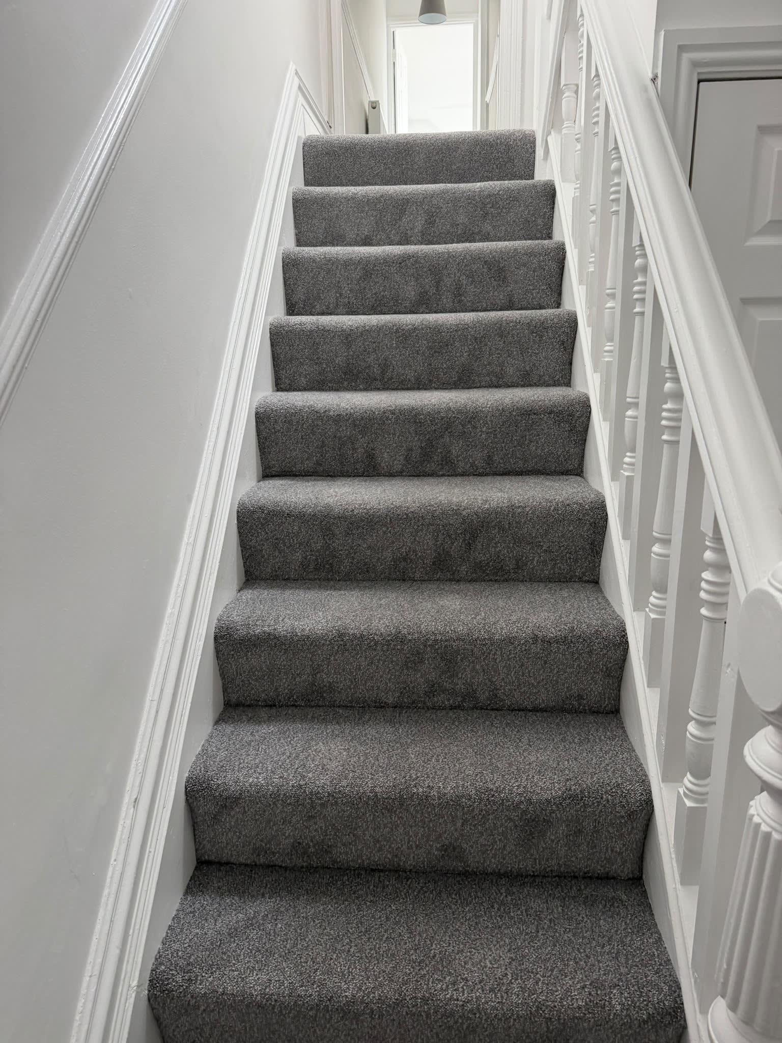 Grey carpet fitted up a straight staircase with white spindles