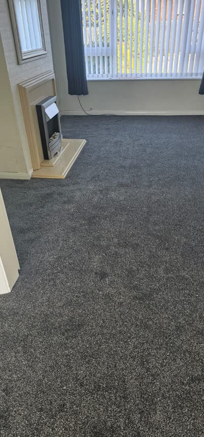 Dark grey carpet fitted in a lounge with a fireplace and vertical blinds