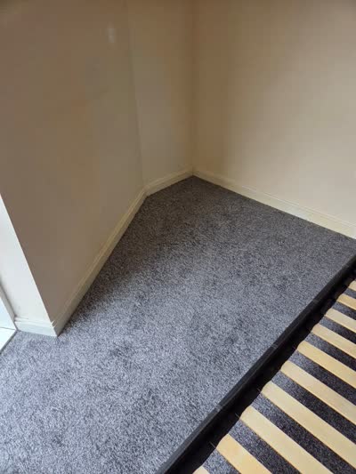 Grey carpet fitted in a bedroom corner beside a bed base