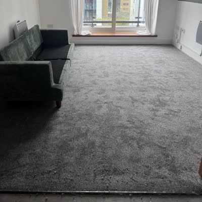 Grey carpet fitted in a living room with a green sofa beside balcony doors