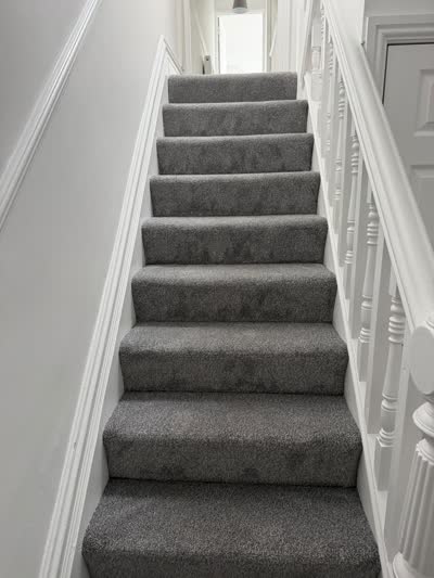 Grey carpet fitted up a straight staircase with white spindles